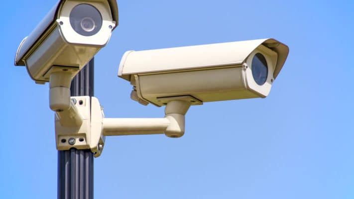 White CCTV cameras on a black post against a blue sky