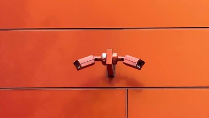 Two CCTV cameras mounted on an orange wall
